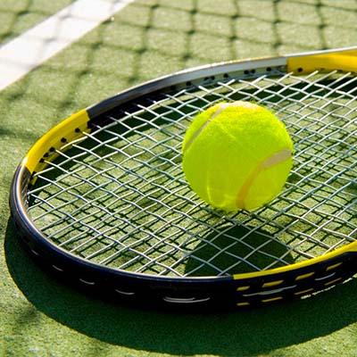 Une balle de tennis reposant sur une raquette sur un court ensoleillé.